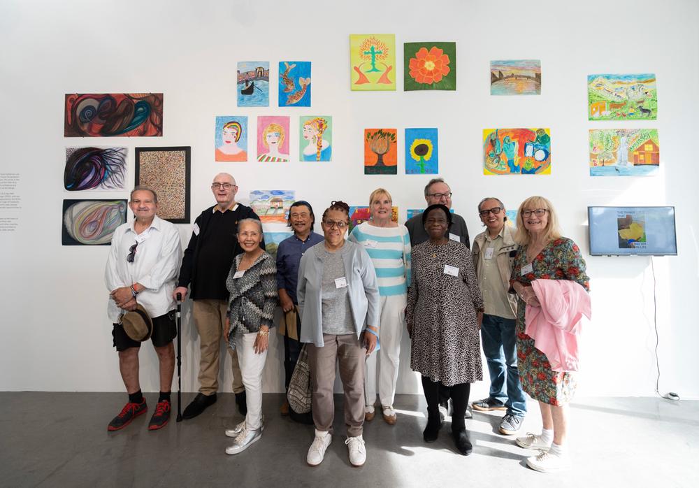 Elders artists in front of white wall with their colorful artworks